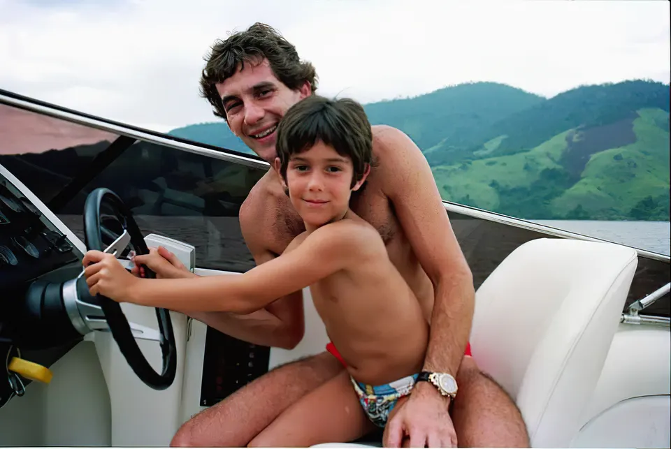 Ayrton Senna ao leme da sua lancha Intermarine Panther 33, sorrindo, com uma criança no colo e a costa ao fundo